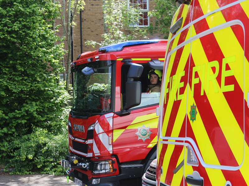 Firefighter sat in a fire appliance with the window down, looking out.