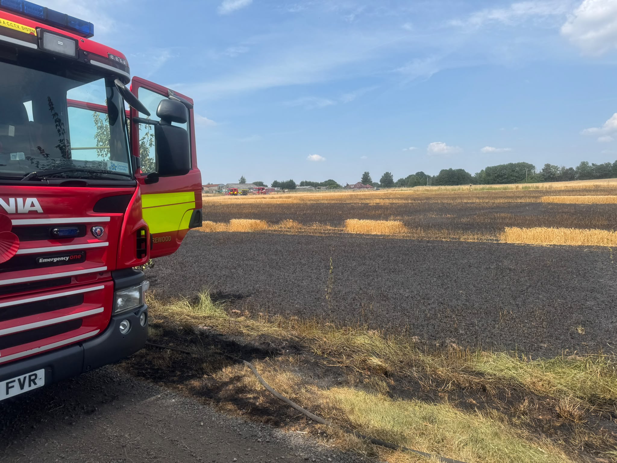 Staffordshire fire engine with the driver door open parked up in front of a burnt crop field on a sunny day
