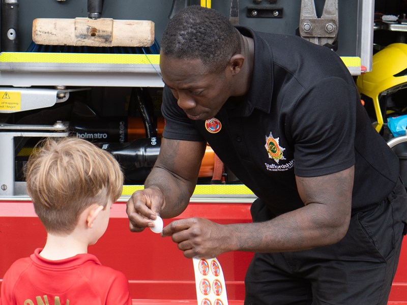 Firefighter giving a Welephant club sticker to a young boy at a community event.